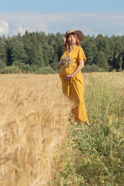 举行在一个阳光明媚的夏日 一位年轻漂亮的孕妇穿着黄色的裙子 戴着黄色的帽子 走过一片麦田父母农村太阳