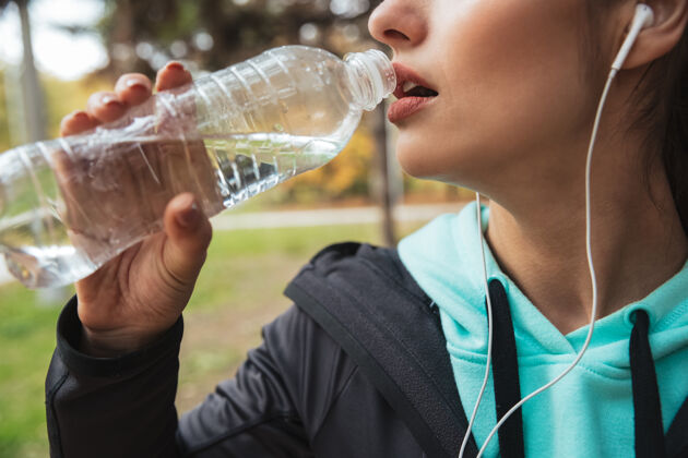 跑步特写镜头：一位健身女士站在公园边用耳机听音乐 手里拿着一瓶水个人资料活动健身