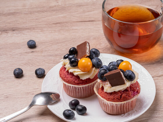 浆果两个自制的水果蛋糕和巧克力放在一个白色的盘子里 一个圆形的茶杯放在一个木制的盘子里餐桌早餐在家里家庭烘焙早餐奶油