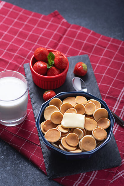 烹饪趋势时髦的小麦片煎饼 蓝色碗里有一片黄油 草莓 红色碗里有一杯牛奶传统的烘焙健康食品