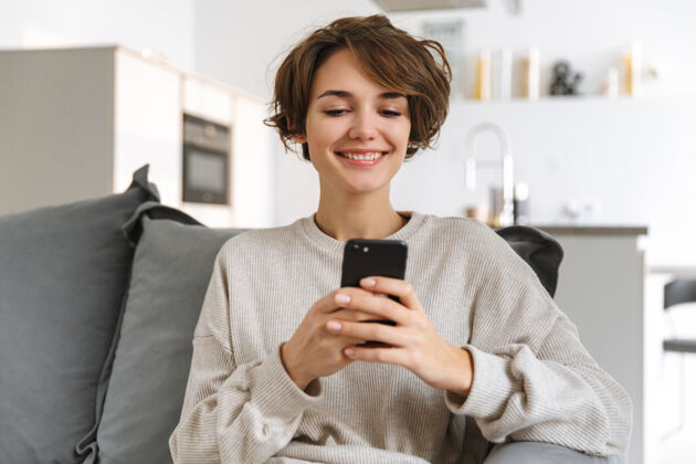 应用程序快乐的年轻女子坐在家里的沙发上 用手机拨号室内景点