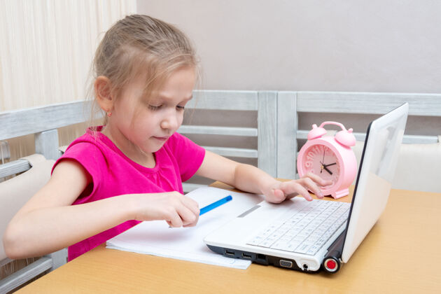 小学生一个可爱的小女孩正坐在桌子旁 用笔记本电脑打作业 交给老师复习时间互联网测试
