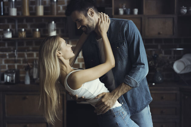 男人美丽的年轻夫妇在厨房跳舞时面带微笑地看着对方支持欢呼女性