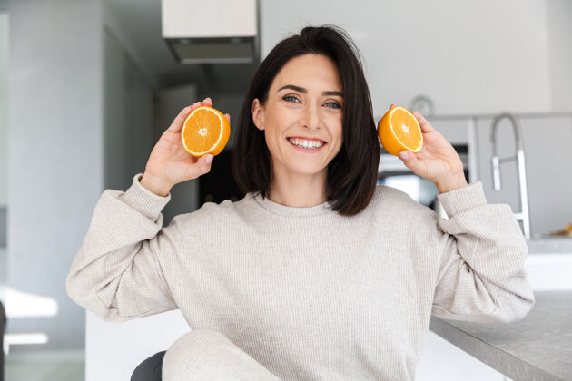 愉快30多岁的黑发女人拿着两片橘子 坐在客厅里沙发肖像件