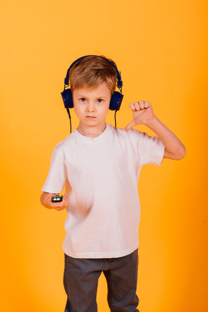 欢呼小男孩戴着耳机听音乐 黄色的背景.儿童耳机里的童话故事孩子拇指朝下情感