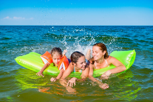 女儿快乐的年轻家庭积极的妈妈和两个小女儿在一个阳光明媚的夏天在海边的黄色气垫上游泳海一起休闲
