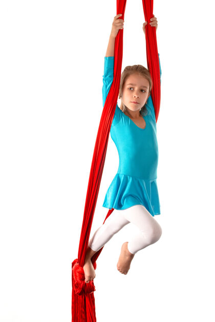 设备一个穿着蓝色泳衣的高加索小女孩 在白色沙滩上的红色飘带上做体操吊床平衡体操