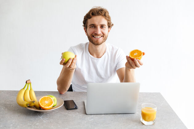 放松快乐的小胡子男人在家里的餐桌上用笔记本电脑捧着水果休闲果汁网络