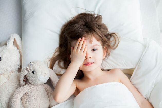 女孩当她醒来时 可爱的小女孩把脸藏在双手后面小手毯子