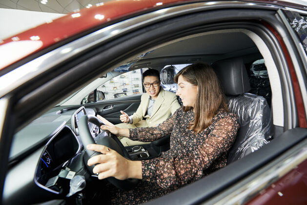 客户坐在汽车沙龙里和推销员一起测试新车的年轻女子运输司机沙龙