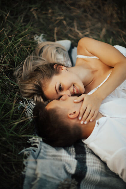年轻一对年轻幸福的夫妇躺在草地上的毯子上草它们在户外野餐毯上放松欢呼季节花园