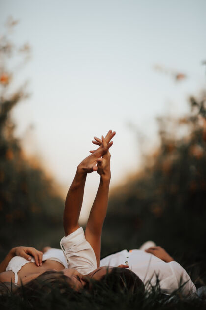 抱着一对放松的年轻夫妇躺在绿色的草坪上 闭着眼睛 手牵着手接吻金发户外乡村