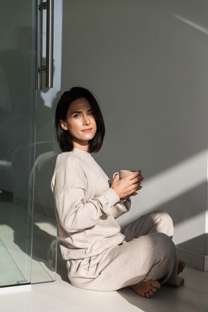 肖像美丽的年轻女子坐在卧室里喝咖啡早餐享受饮料