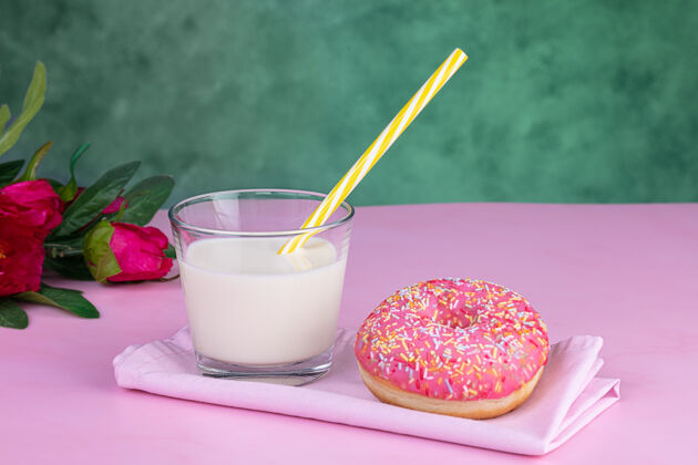 糕点粉红色的甜甜圈和一杯牛奶在粉红色的表面洒圈甜甜圈