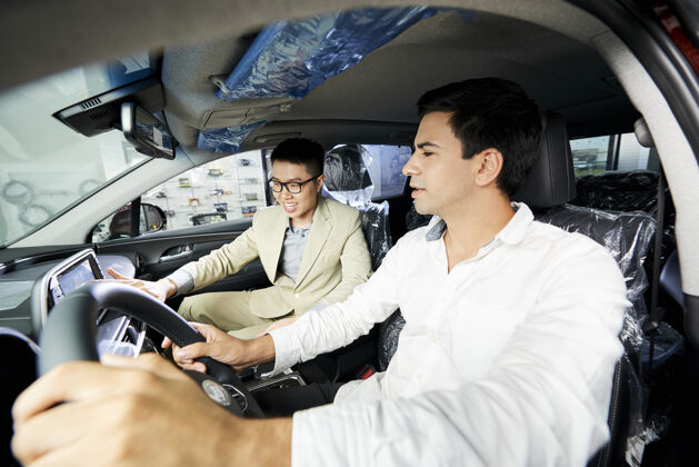 车年轻人买了一辆新车 他和亚洲推销员一起坐在汽车沙龙里测试一辆新车司机新解释