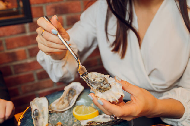 烹饪一双白种人的手平放在一张深色的桌子上 手里拿着牡蛎和其他海鲜菜肴冷咖啡馆晚餐
