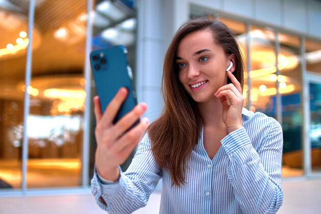 电话现代快乐休闲聪明的千禧一代女性戴着无线耳机用智能手机进行视频通话和远程在线聊天移动观看移动