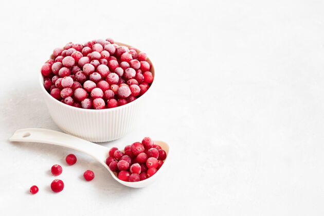 勺子把冰冻的红色浆果放在碗里 勺子放在白色的背景上带霜的小红莓素食文本空间冷冻浆果水果