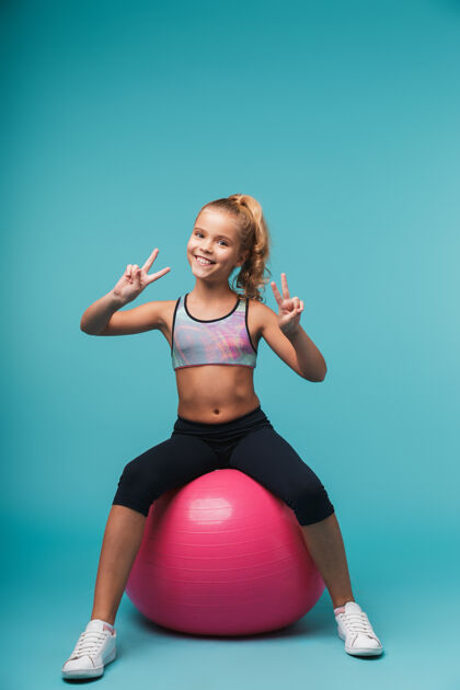 幼儿园快乐的小女孩穿着运动服和健身球隔着蓝色的墙做运动快乐孩子球