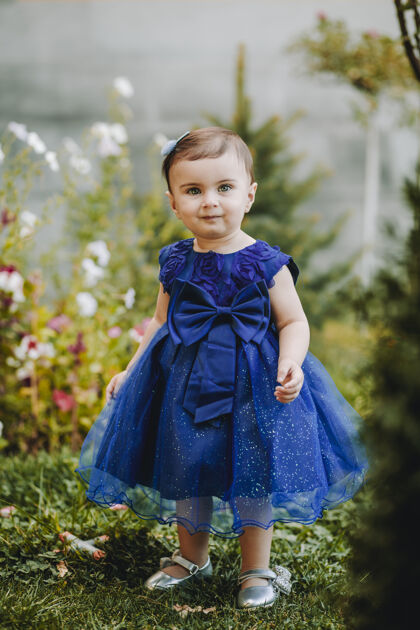 服装可爱的女婴穿着蓝色的裙子站在花园里的草地上 花儿很多女性幼儿可爱