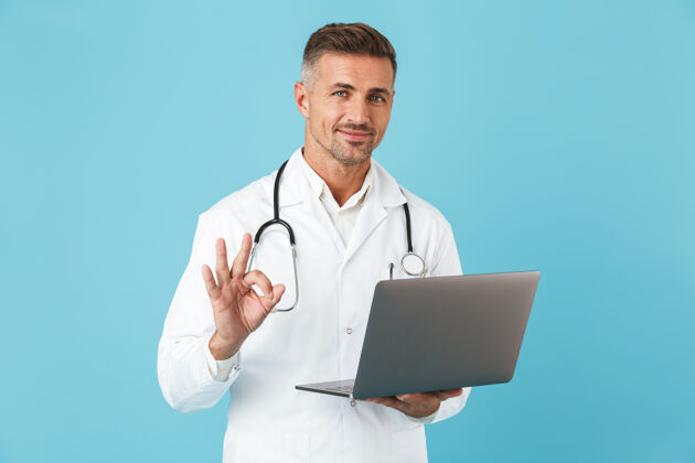 心脏病专家专业医生身穿白大褂 手持手提电脑听诊器 孤立地站在蓝色墙壁上的照片职业中年医生