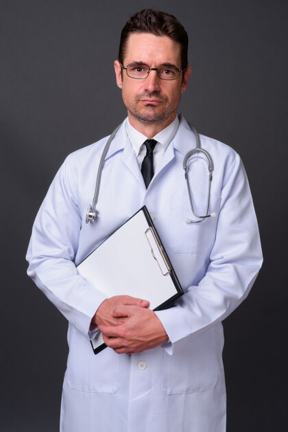 男人长着胡子的帅哥医生戴着眼镜靠着灰墙胡须实验室听诊器