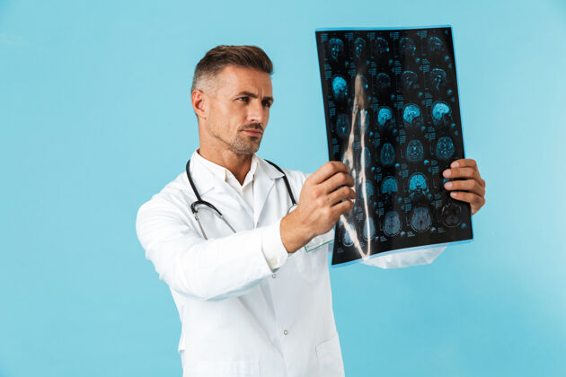 职业带听诊器的严肃医生的肖像 手持x光片 孤立地站在蓝色的墙上救护车情绪表情