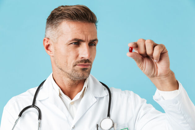 工人一张严肃的医生身穿白大褂 手里拿着一颗药丸 孤零零地站在蓝色的墙上的照片治疗医院听诊器