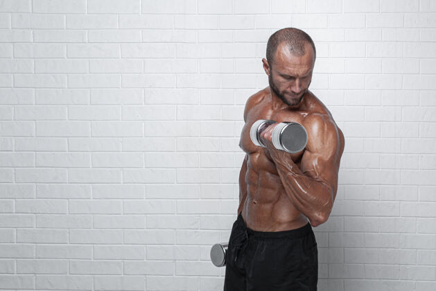 健康健美运动员在砖墙上用哑铃练习二头肌锻炼阳刚身体