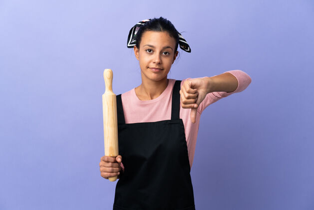 专业穿着厨师制服的年轻女子用否定的表情展示拇指朝下服务消极围裙