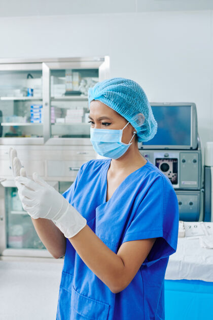 女性严肃的年轻外科助理在手术室里戴上消毒手术手套和医用口罩医疗职业研究工作