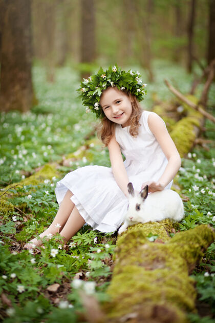 欢呼穿着白色连衣裙的漂亮小女孩 在春天的树林里和白兔在一起活动农场可爱