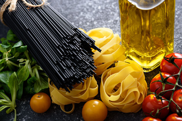 饮食特写意大利食品配料意大利面 费图西尼 黑意大利面 西红柿 香草和绿松石背景上的橄榄油瓶 烹饪晚餐的概念意大利意大利乡村