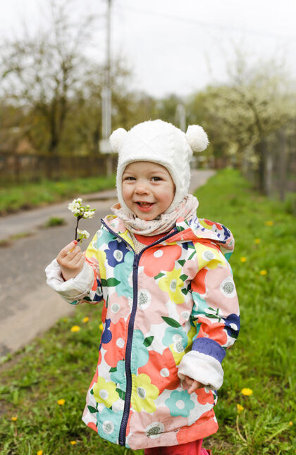 欢乐一个穿着鲜艳夹克的小女孩在外面的春天里开心地笑着 手里拿着一根春白的树枝花孩子我的幸福肖像年轻抱着