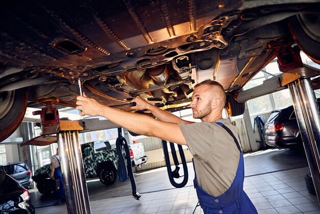 工作帅气的汽车修理工在加油站检查汽车的传动装置控制调谐技师