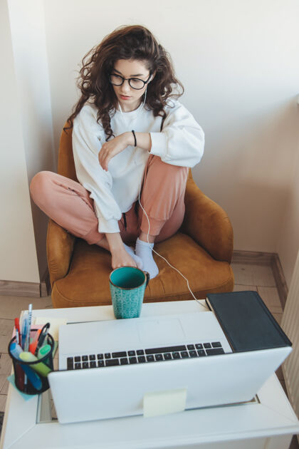 教育一位戴眼镜的卷发女士正在家里用笔记本电脑上网络课 喝着茶学生写作女孩
