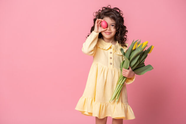节日有趣的小女孩拿着郁金香和五颜六色的复活节彩蛋在她眼前的粉红色童年郁金香复活节