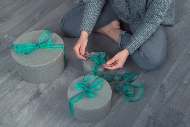 礼物女人用灰色的圆盒子和绿色的丝带包装礼物坐着工艺女士