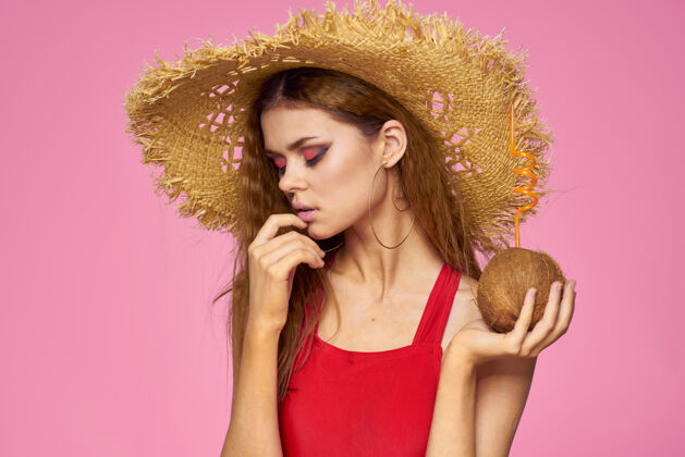 时尚戴着草帽的椰子鸡尾酒的女人异国情调的度假夏日粉色的墙壁成人泳装性感