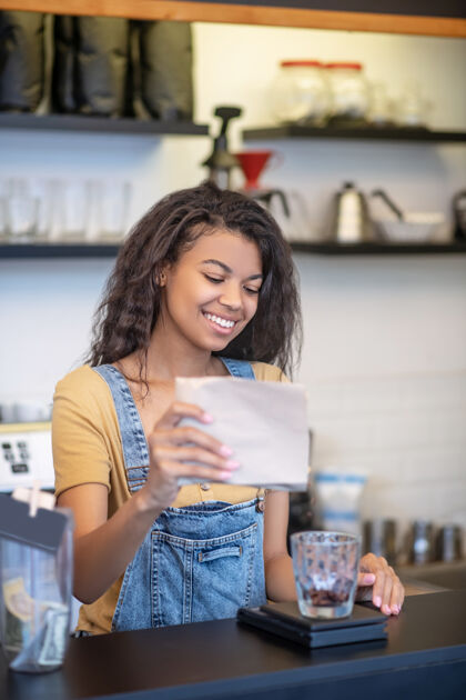 订单出售咖啡微笑站在咖啡馆的吧台后面 一位留着黑色长发的年轻女子正在往杯子里倒咖啡豆长发欢乐测量