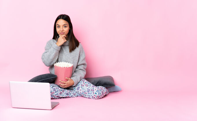 聪明年轻女子一边吃爆米花一边在笔记本电脑上看电影一边思考年轻想法节目