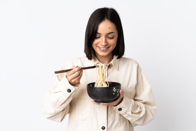 举行年轻的白种女人用筷子端着一碗面条 孤零零地站在白色的地面上食物中国墙