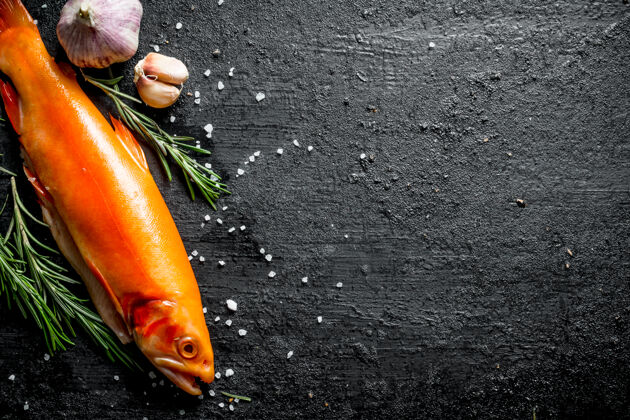 配料生鱼鳟鱼配迷迭香和大蒜放在黑色乡村餐桌上动物生的营养