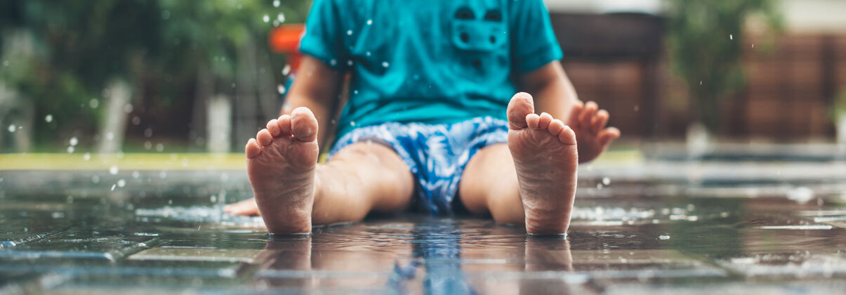 情绪一个穿着蓝色衣服赤脚坐在水里玩耍的白人小男孩的无脸照片滴水脚地板