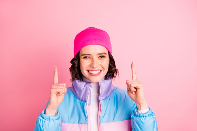 Hipster好女人的照片表明举手空位穿暖色外套隔离粉红色背景StudentChearCoat