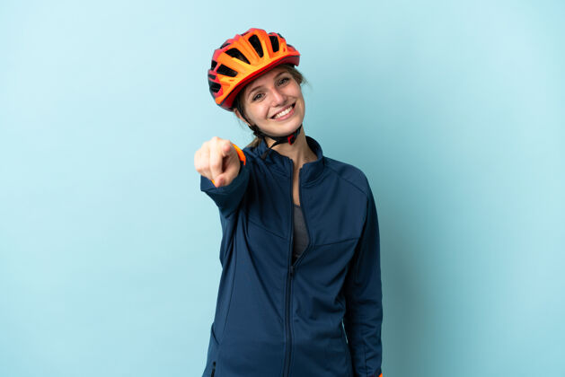 前面年轻的骑自行车的女人孤立在蓝色的背景 指着前面的快乐表情女孩震惊女人