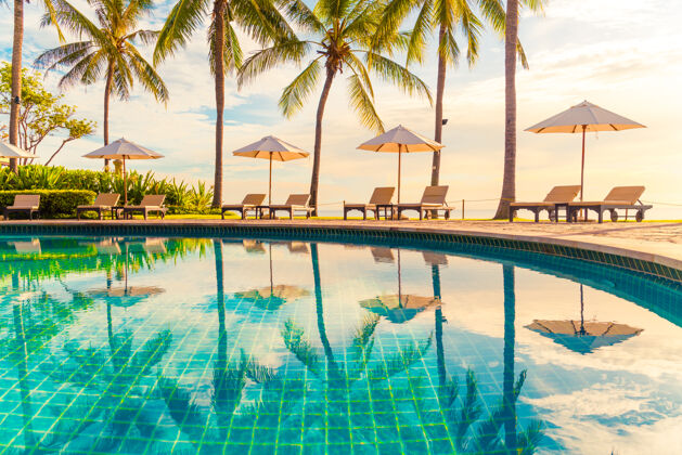 海滩美丽的豪华伞和椅子周围的室外游泳池在酒店和度假村椰子棕榈树日落或日出天空假日还有度假的概念日出海洋黎明