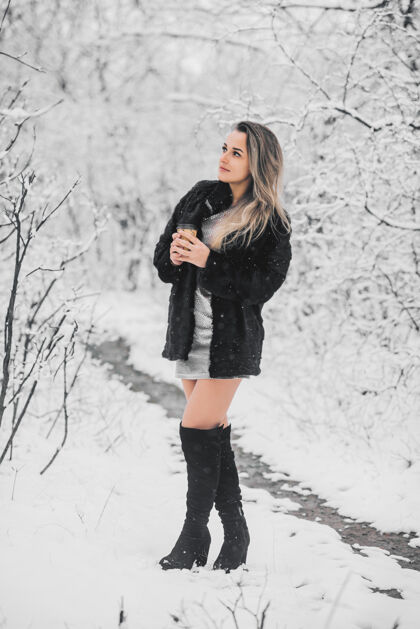 欢乐冬天在森林里 一个穿着皮衣长裙和高筒靴的漂亮女孩手里拿着咖啡女孩心情森林