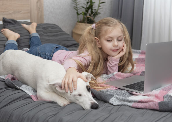 在一起金发女孩在家上网学习笔记本电脑.儿童还有一只狗在床上孩子狗平板电脑