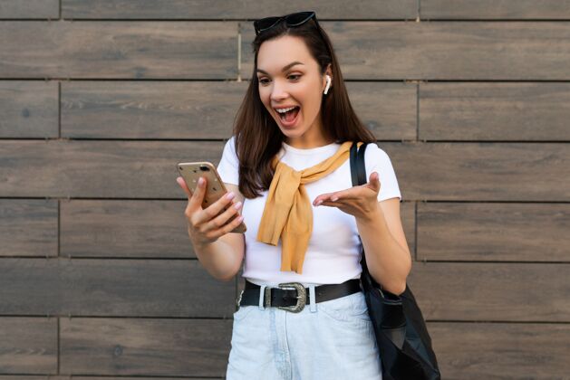 电话一位穿着休闲服的年轻女子站在街上 通过手机进行交流 看着智能手机 心情愉快交谈年轻互联网